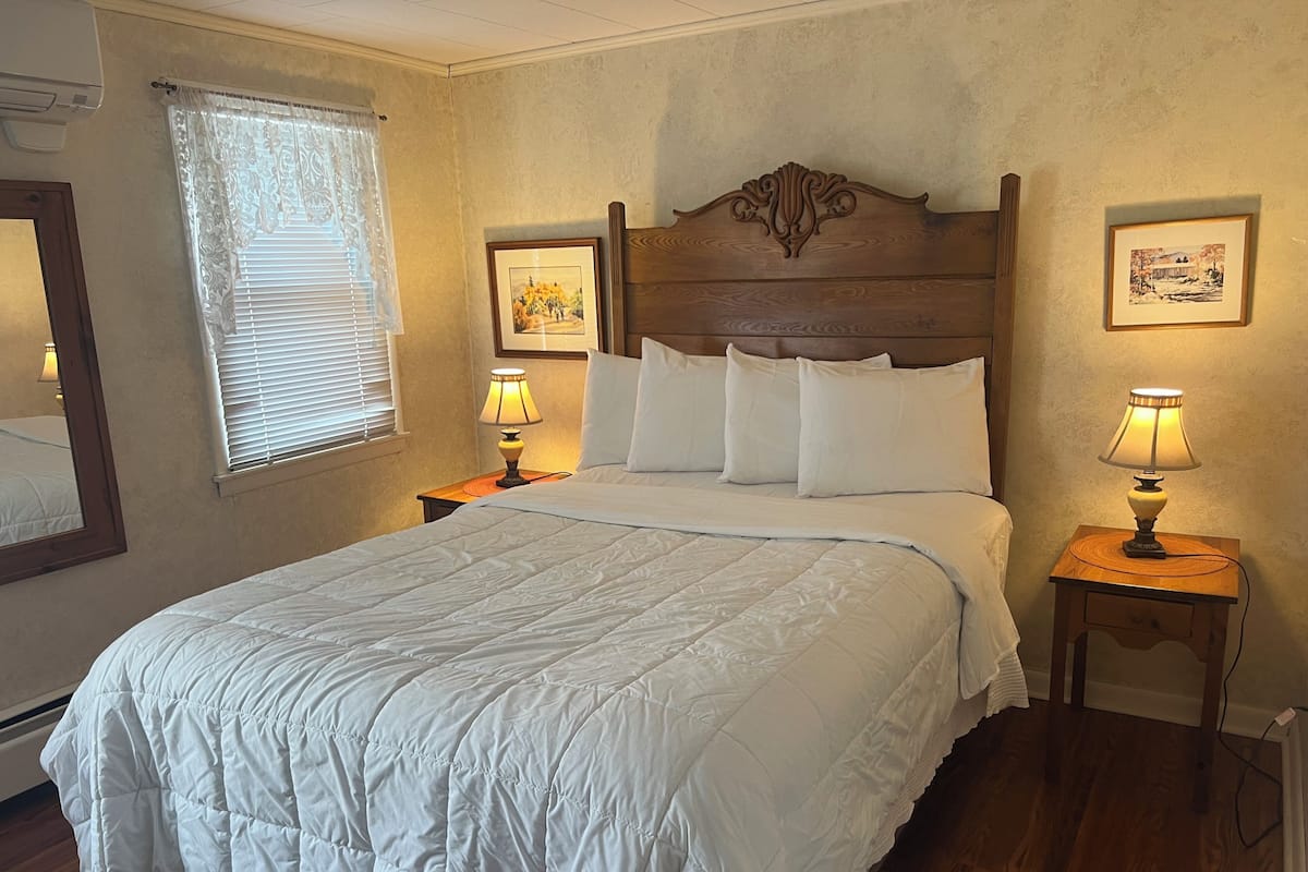 Cama bem arrumada com roupa de cama branca, duas luminárias de cabeceira e cabeceira de madeira.