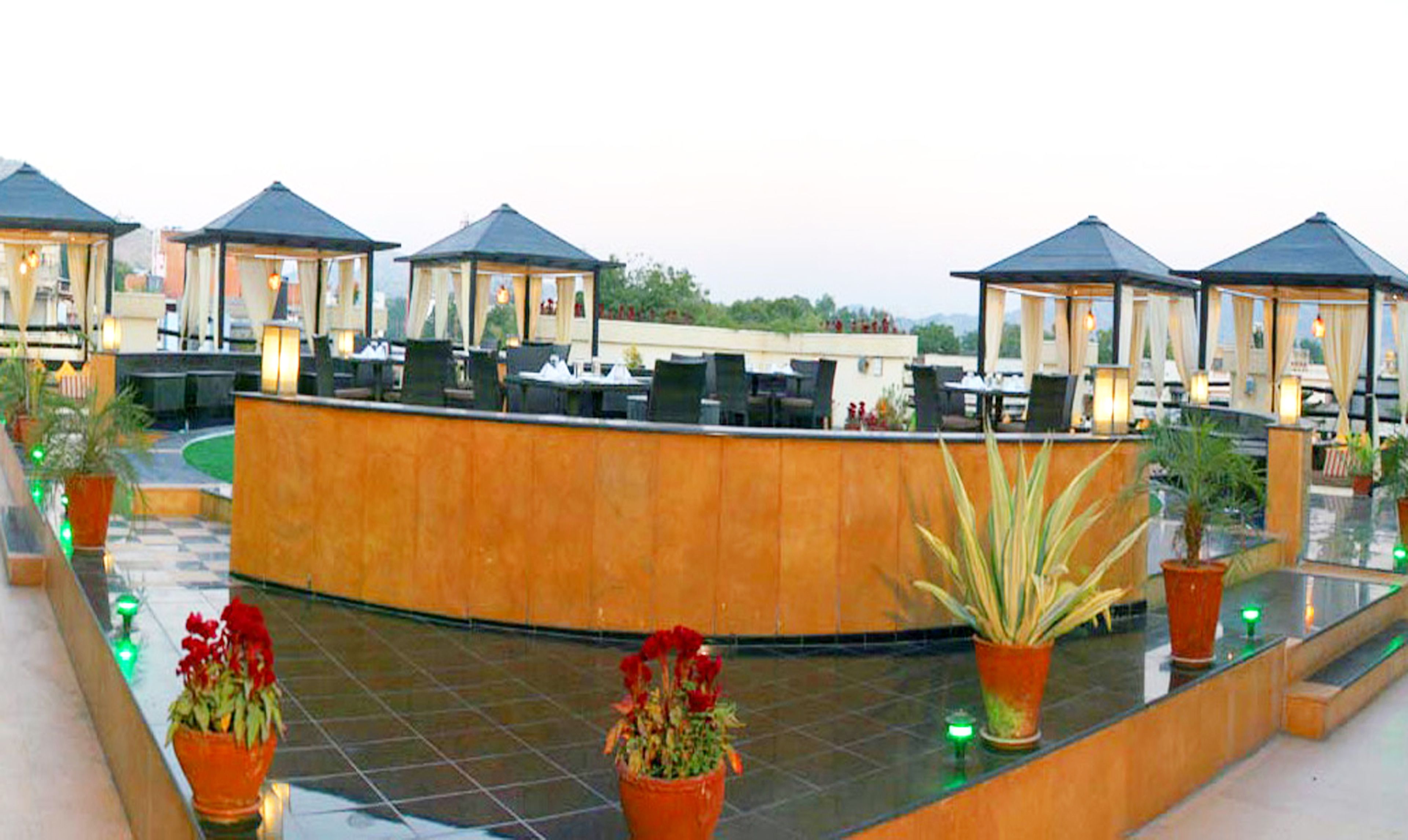 A rooftop terrace with multiple seating areas, potted plants, and a central reception desk.