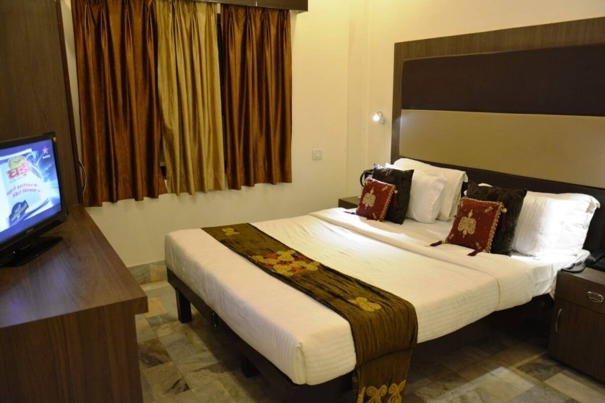 A hotel room with a bed, a television on a wooden table, and curtains on the window.