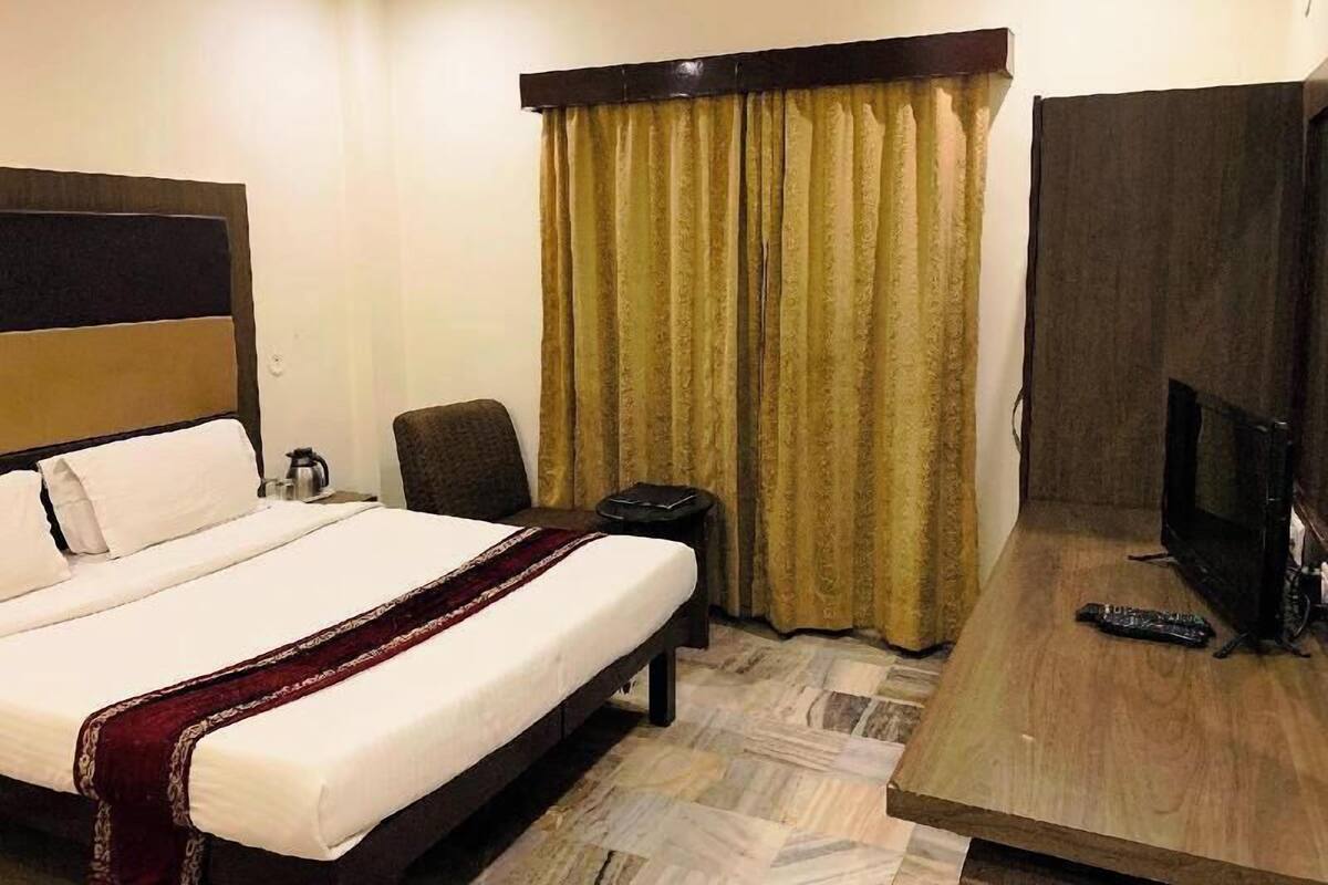 A hotel room with a bed, a chair, a TV, and a curtain.
