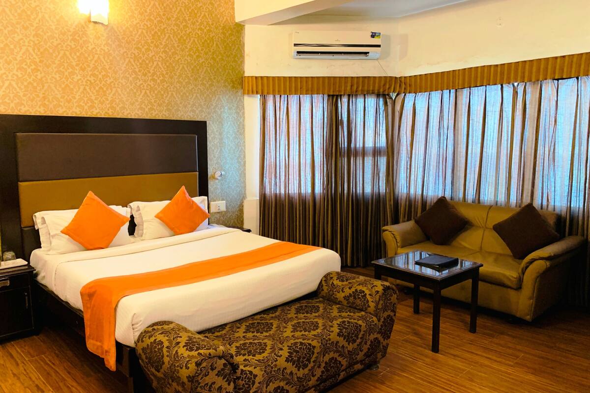 A hotel room with a large bed, a sofa, a small table, and a patterned armchair.
