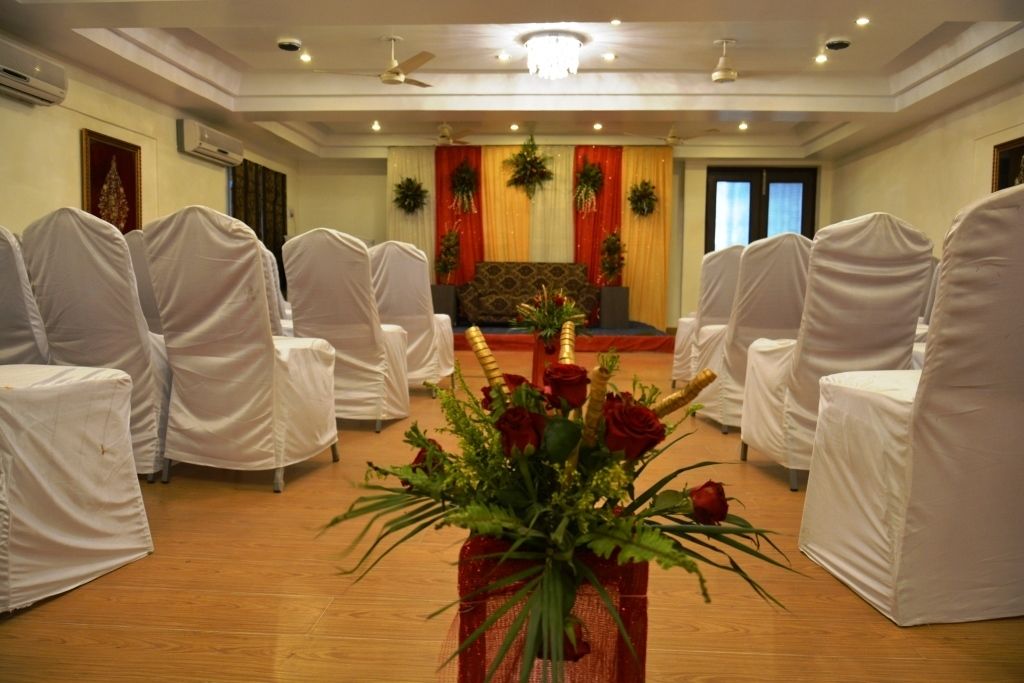 A conference room with rows of white-covered chairs facing a stage with red and gold drapes.