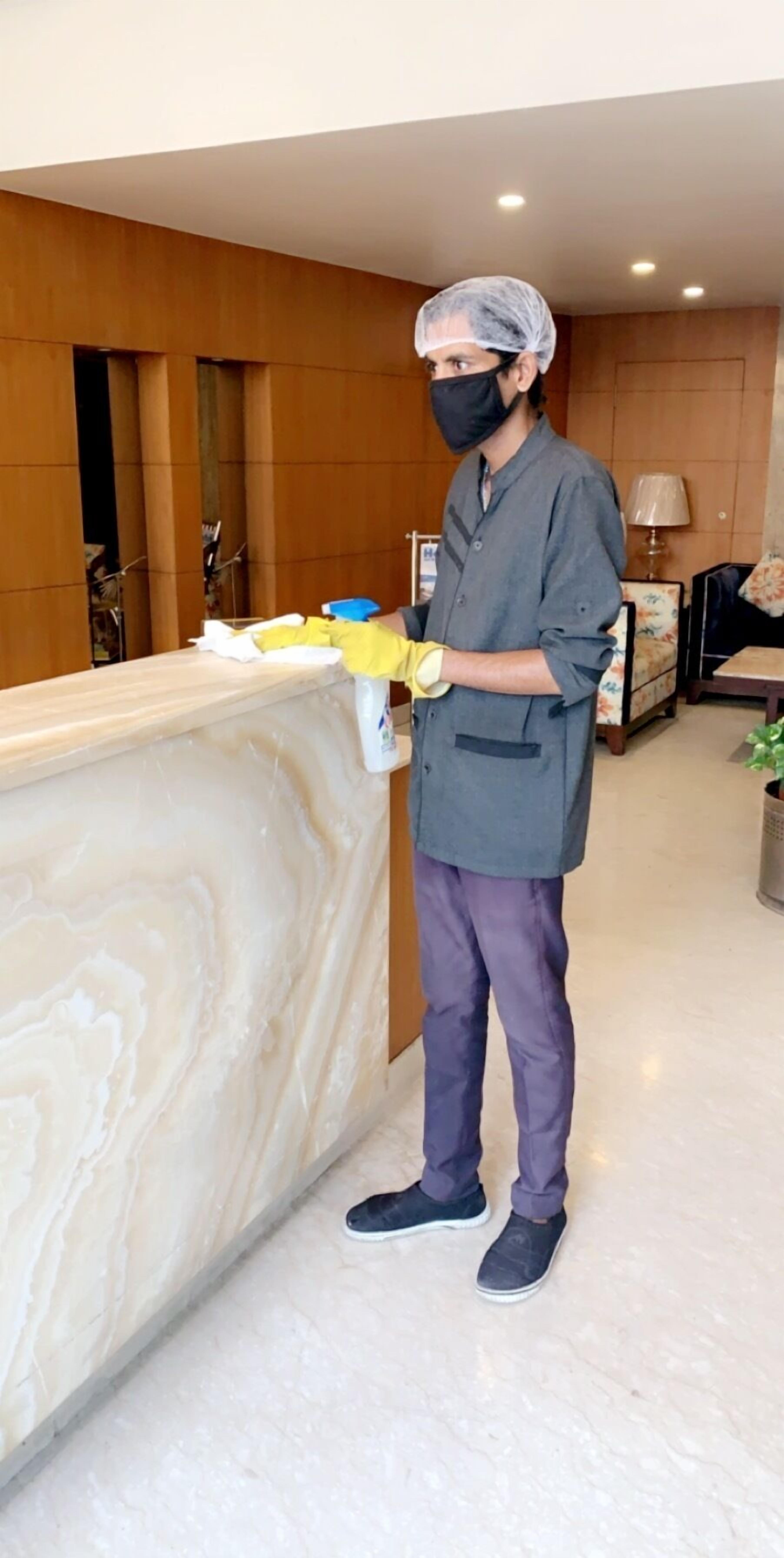 A person cleaning a marble reception desk in a hotel lobby with wooden paneling and a lamp in the background.