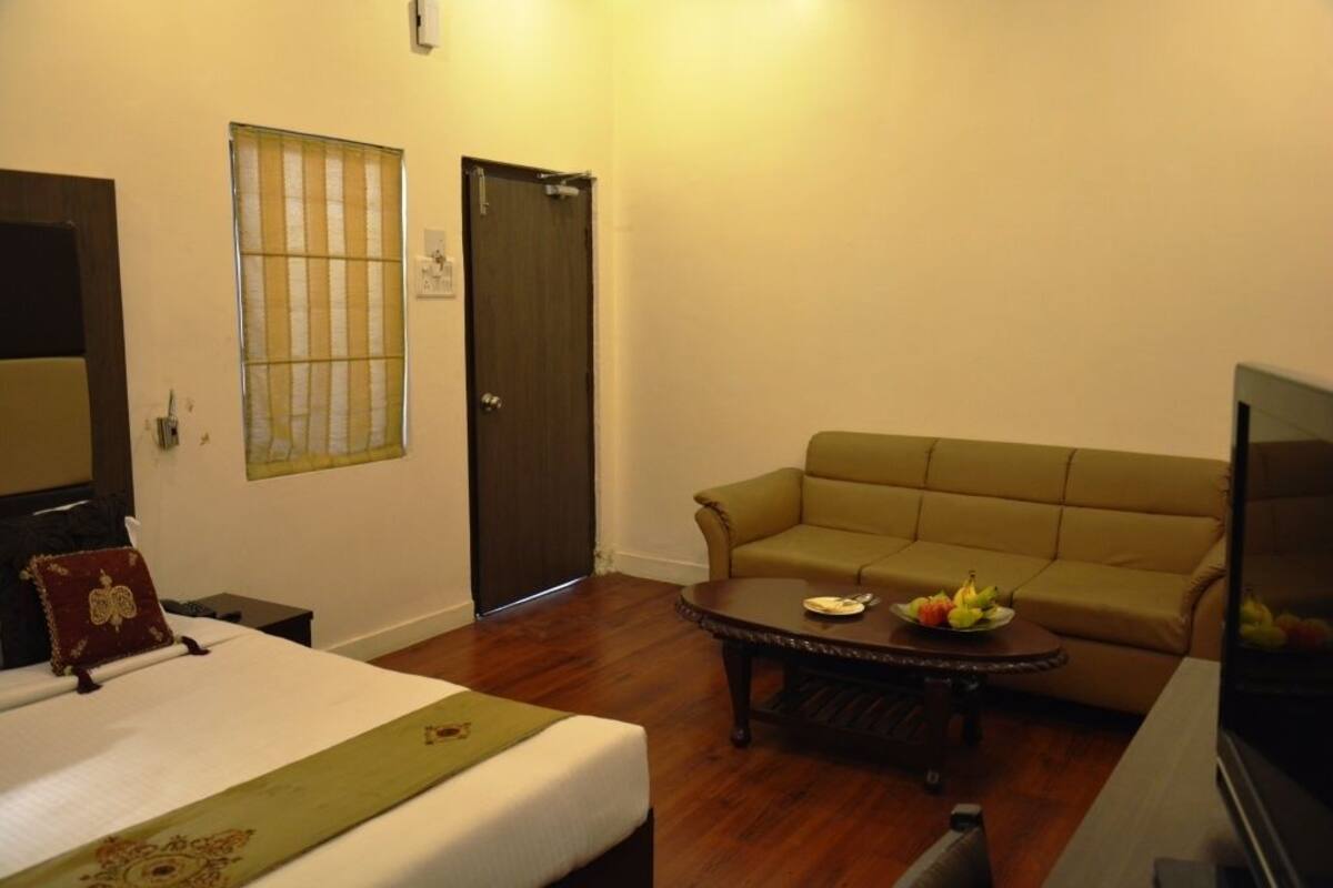 A hotel room with a bed, a sofa, a coffee table with fruit, and a TV.