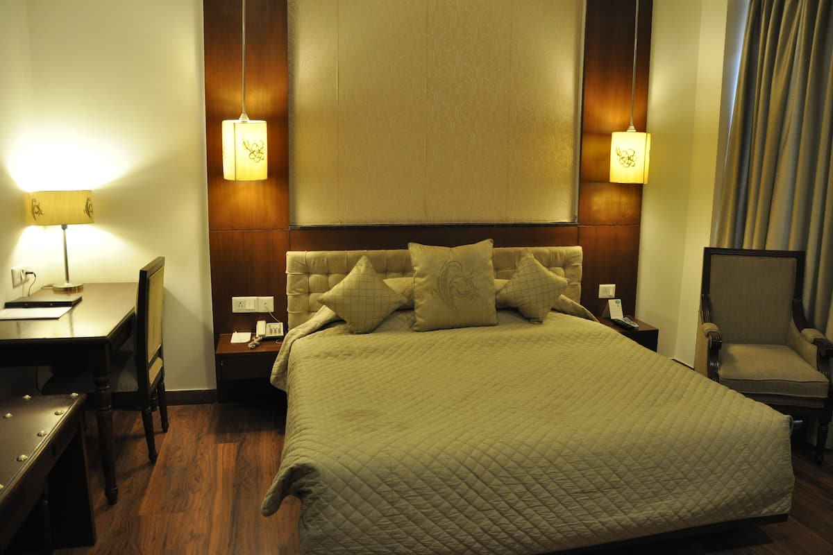 A hotel room with a large bed, a desk, a chair, and two bedside lamps.