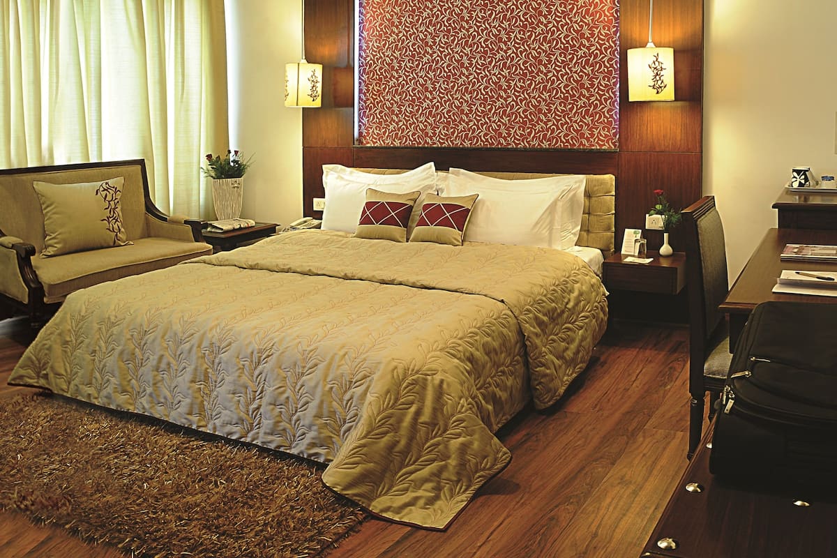 A hotel room with a large bed, a desk, a chair, a nightstand, and a lamp.