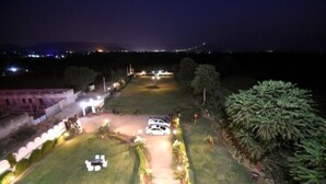 A nighttime view of a hotel courtyard with a white car parked in the center, surrounded by well-lit pathways and greenery. - Satyam Palace Resort (Pushkar)