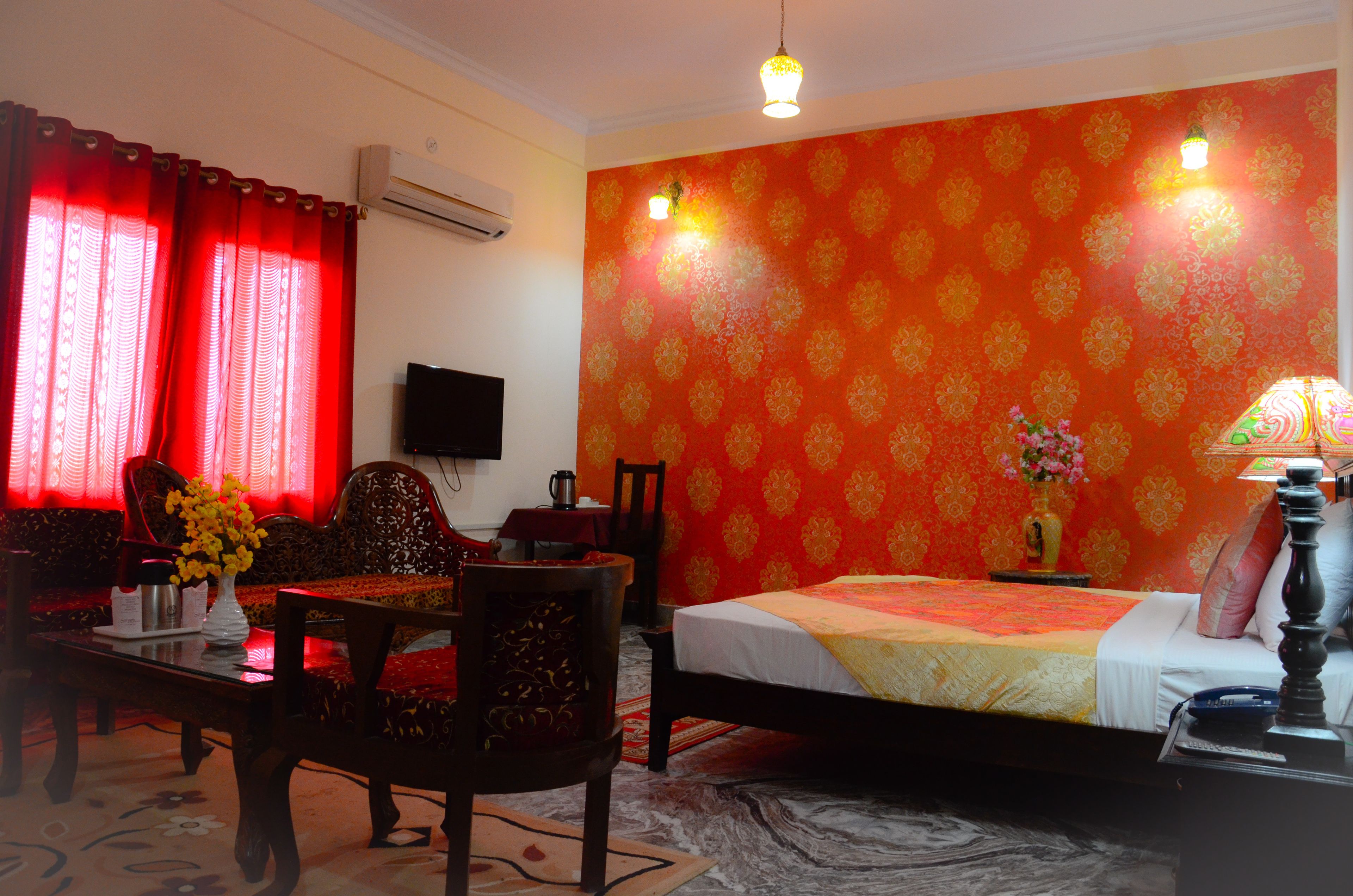 A hotel room with a bed, a TV, a table with a vase of flowers, and a red patterned wall.
