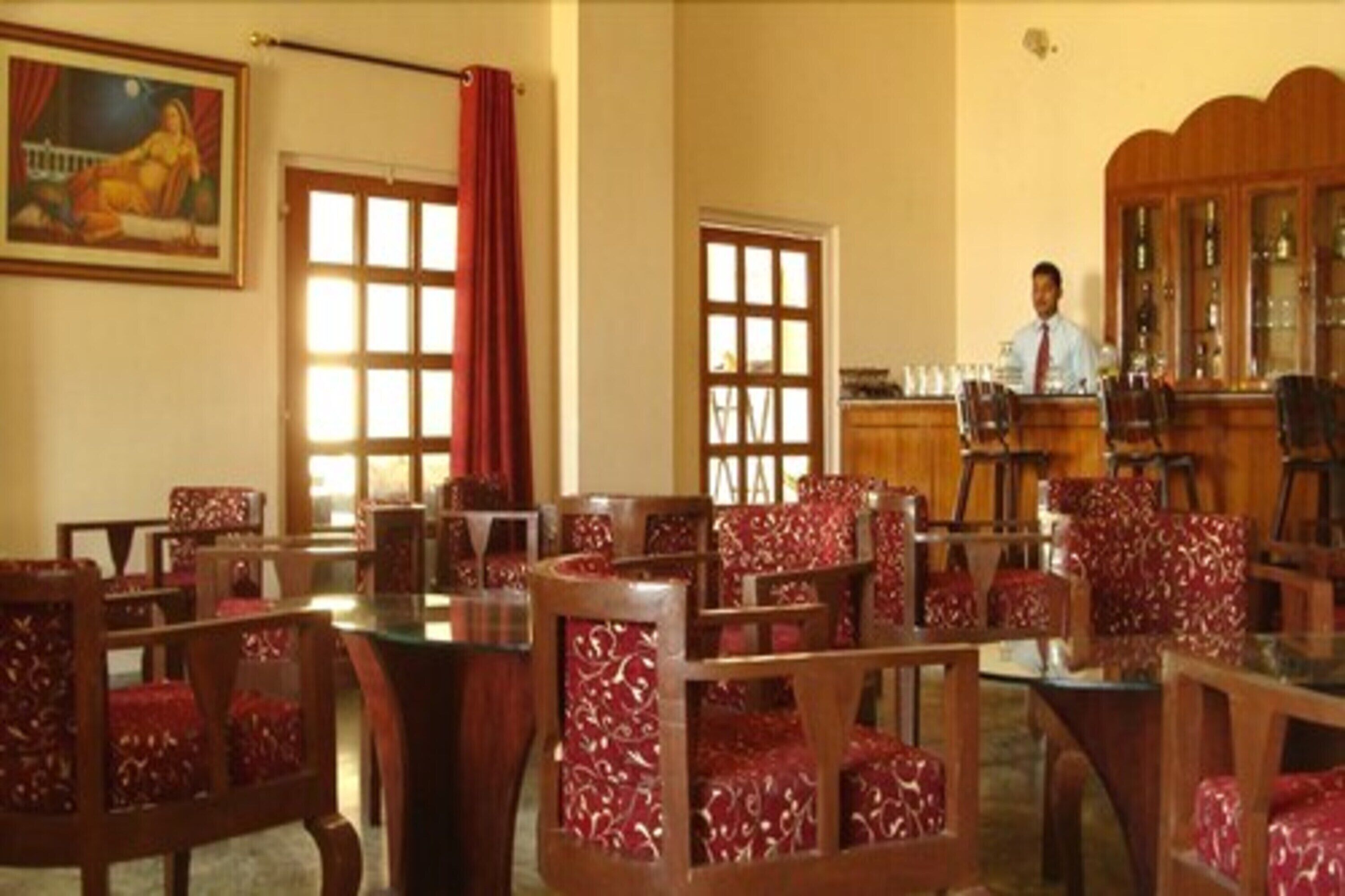 A hotel dining area with wooden furniture and red patterned upholstery. There are multiple tables and chairs arranged for dining.