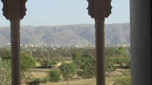A view through a window with ornate columns, a mountainous landscape, and a distant town. - Satyam Palace Resort (Pushkar)