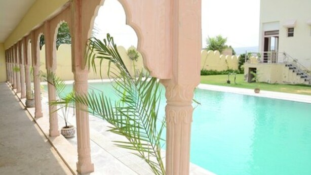 A pool area with a covered walkway, columns, and potted plants. - Satyam Palace Resort (Pushkar)