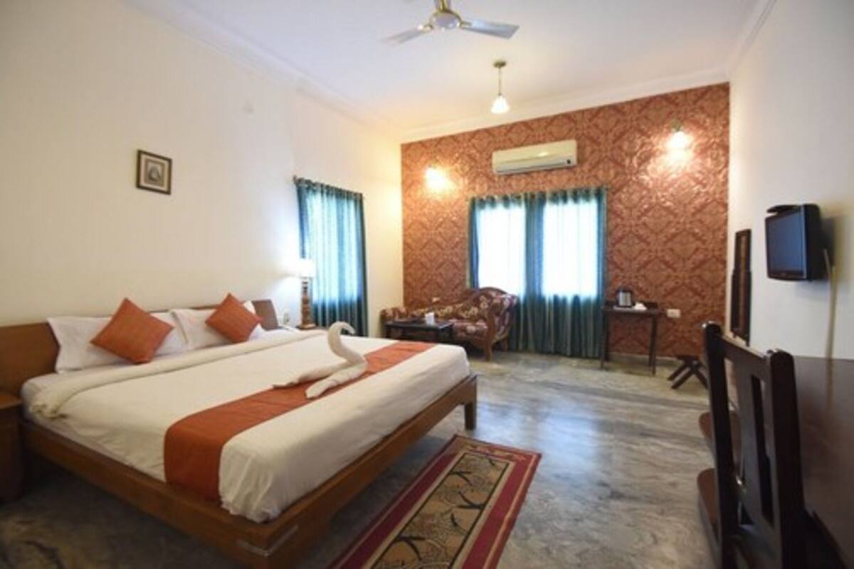 A hotel room with a large bed, a ceiling fan, a TV, and a small table with a chair.