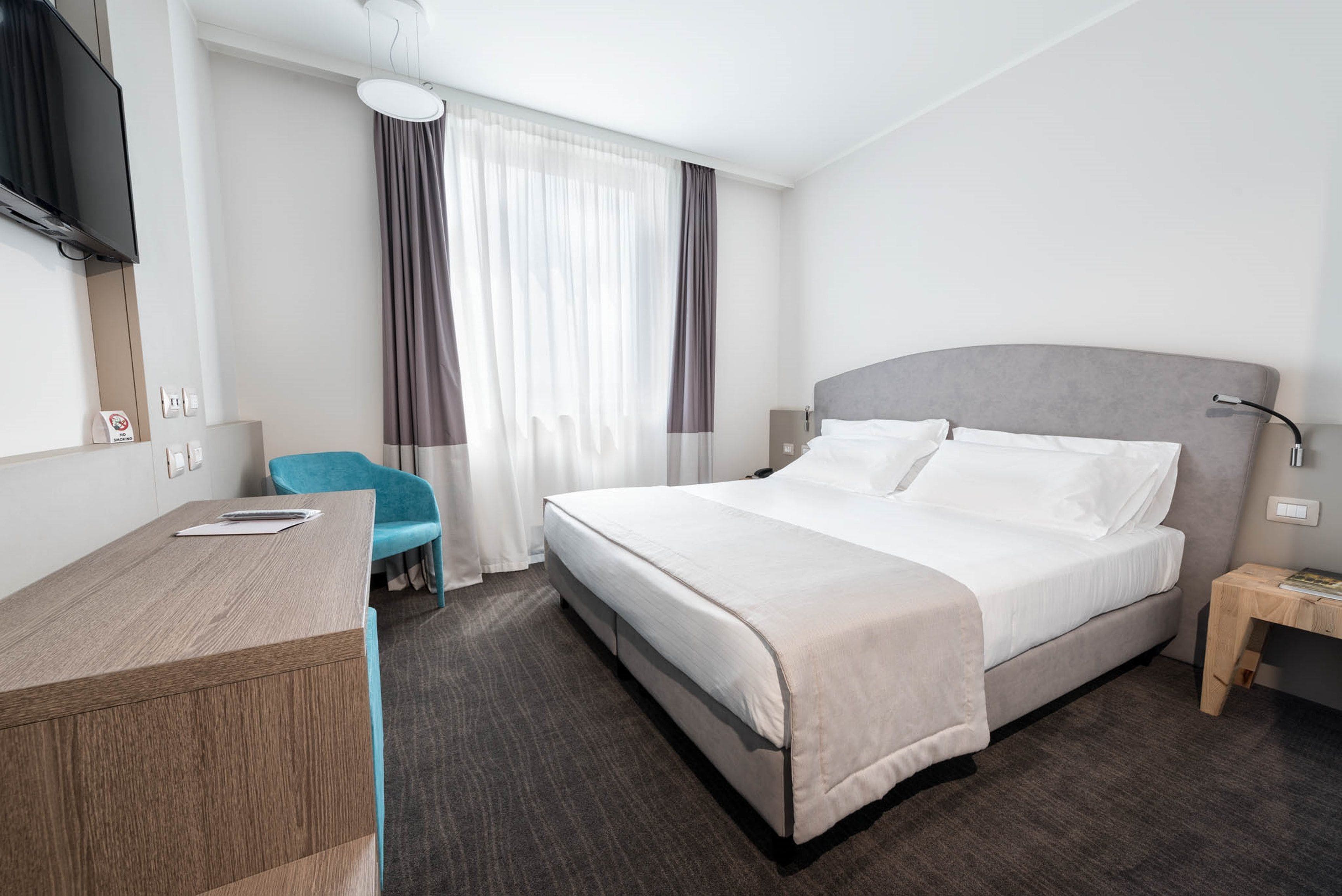 A hotel room with a bed, a desk, a chair, a TV, and a nightstand.