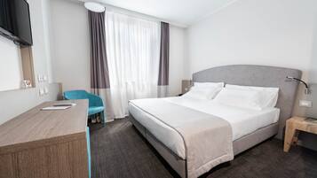 A hotel room with a bed, a desk, a chair, a TV, and a nightstand.