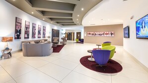Eine moderne Lobby mit gewölbter Decke, einem grauen Sofa, farbenfrohen Stühlen und Kunstwerken an den Wänden.