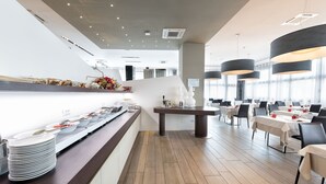 A modern restaurant with a long counter, multiple tables, and hanging pendant lights. -  DB HOTEL VERONA, AIRPORT CONGRESS & SPA (Sommacampagna)