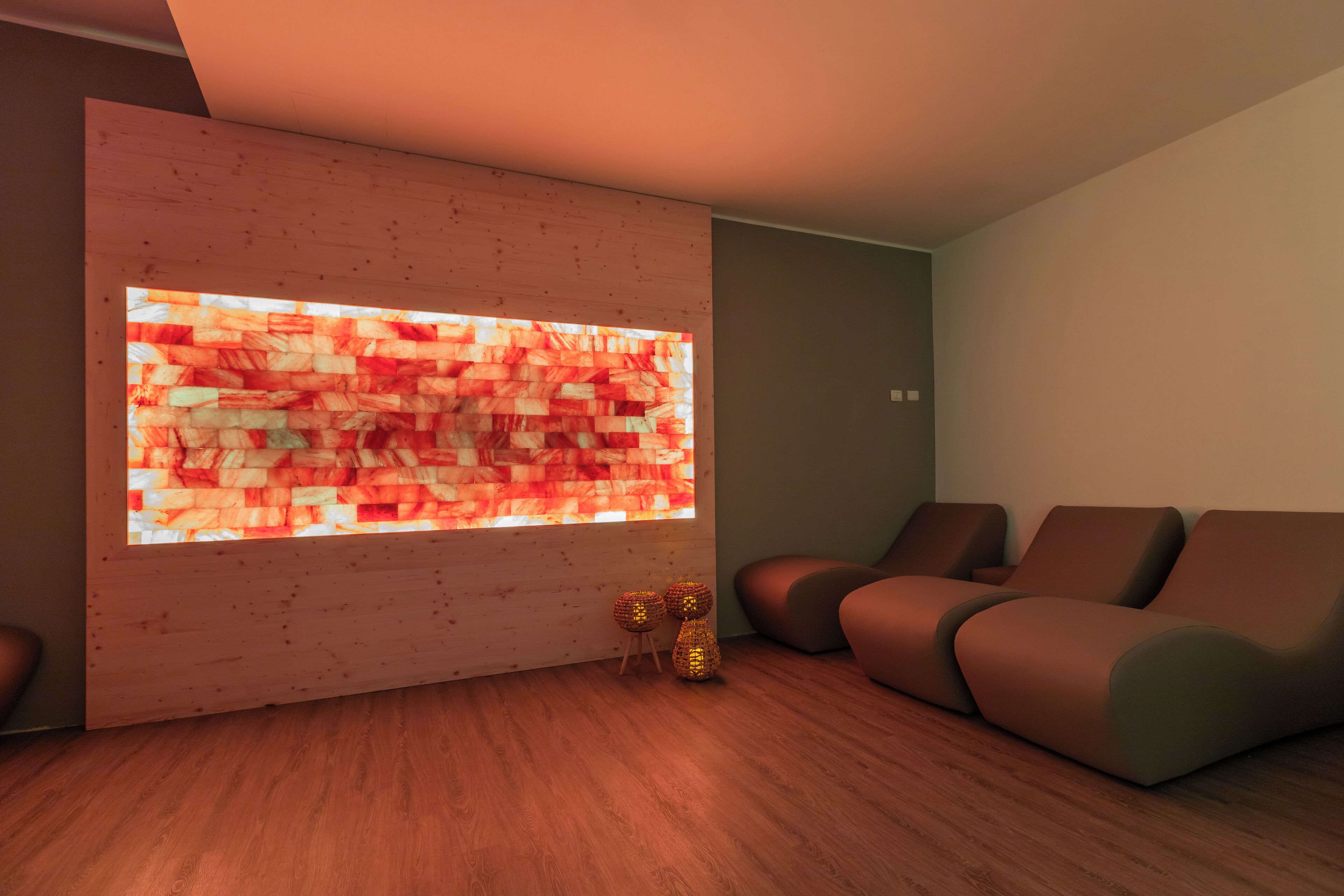 A modern living room with a wooden wall, a large illuminated artwork, and a seating area with cushioned chairs.