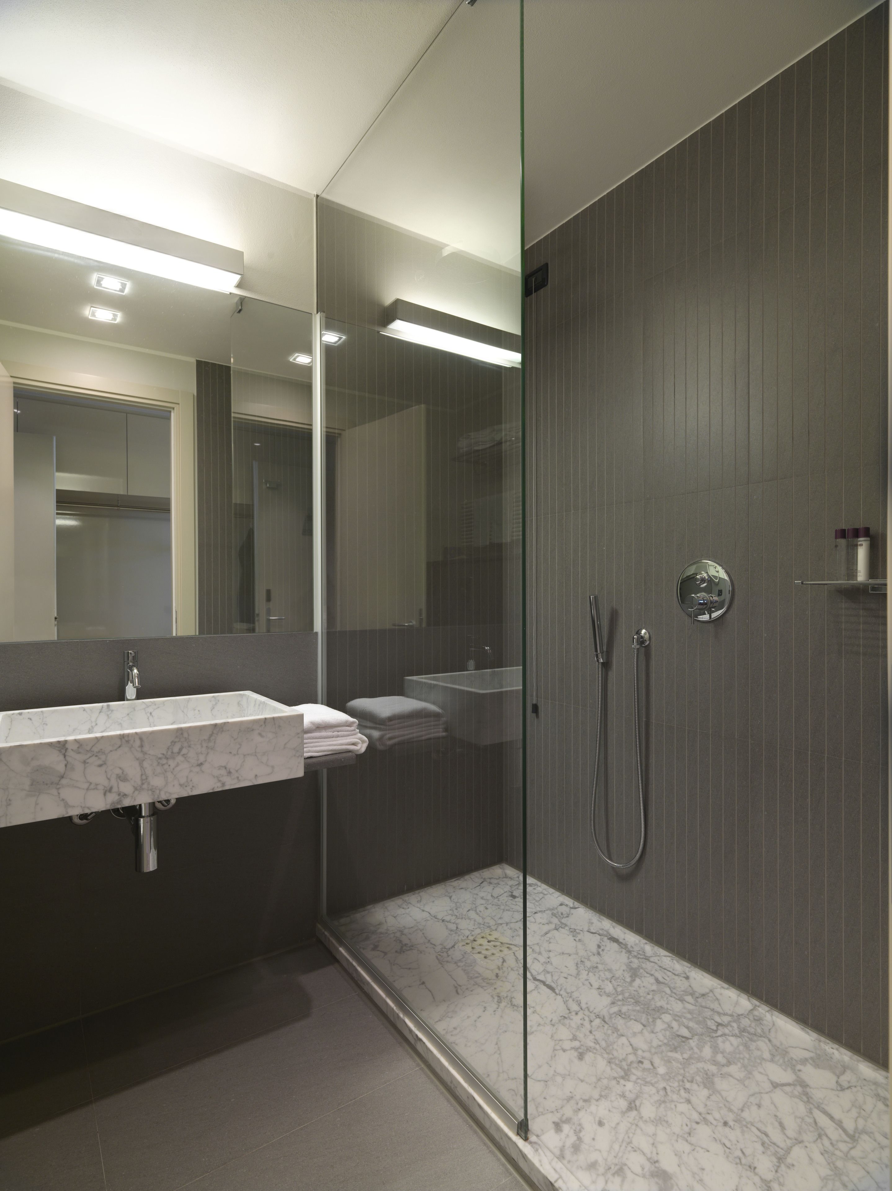 A modern bathroom with a glass-enclosed shower, a marble sink, and a large mirror.
