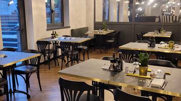 Interior de restaurante con varias mesas y sillas, plantas colgantes e iluminación colgante.