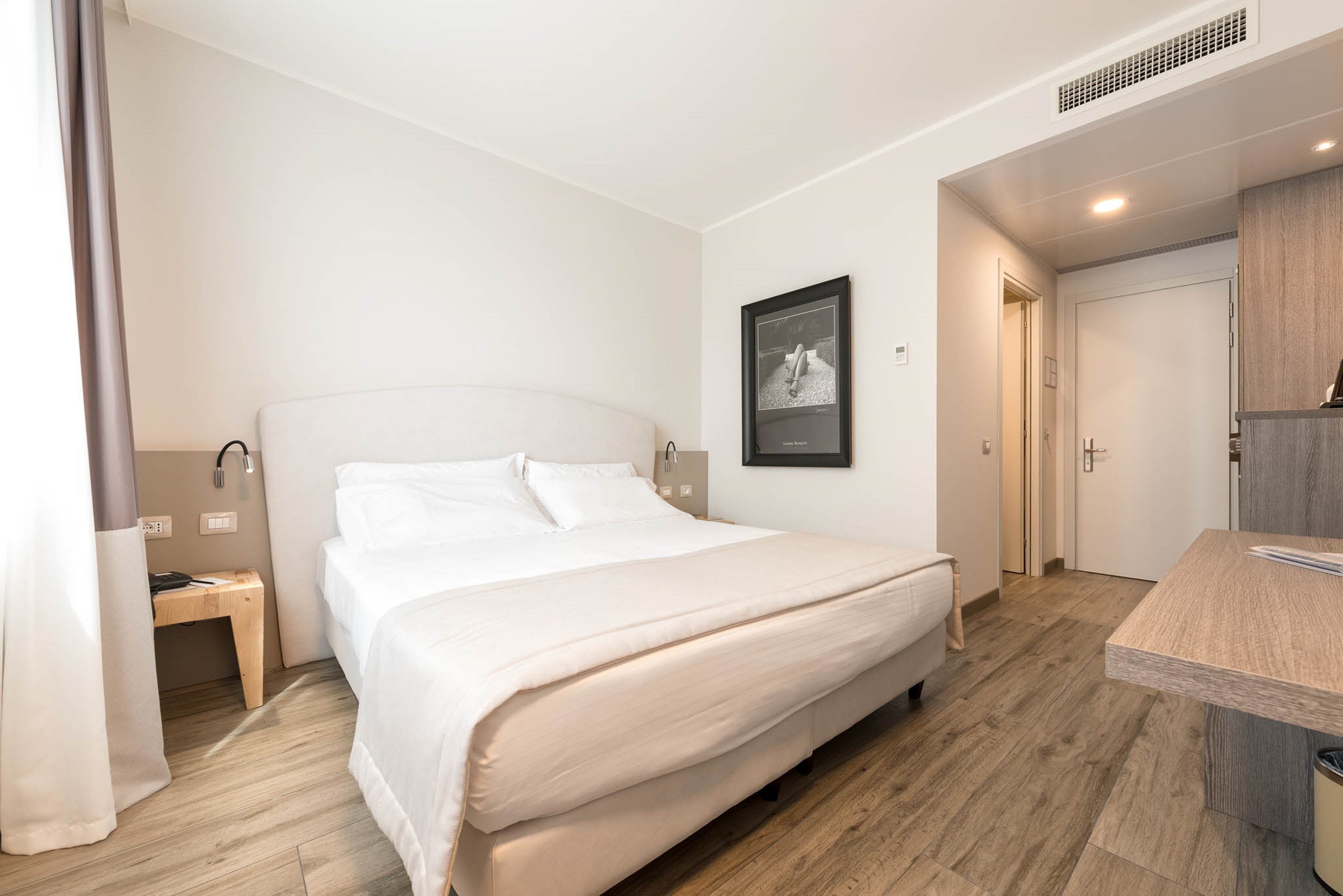 A modern hotel room with a large bed, a bedside table, a desk, and a small bathroom.