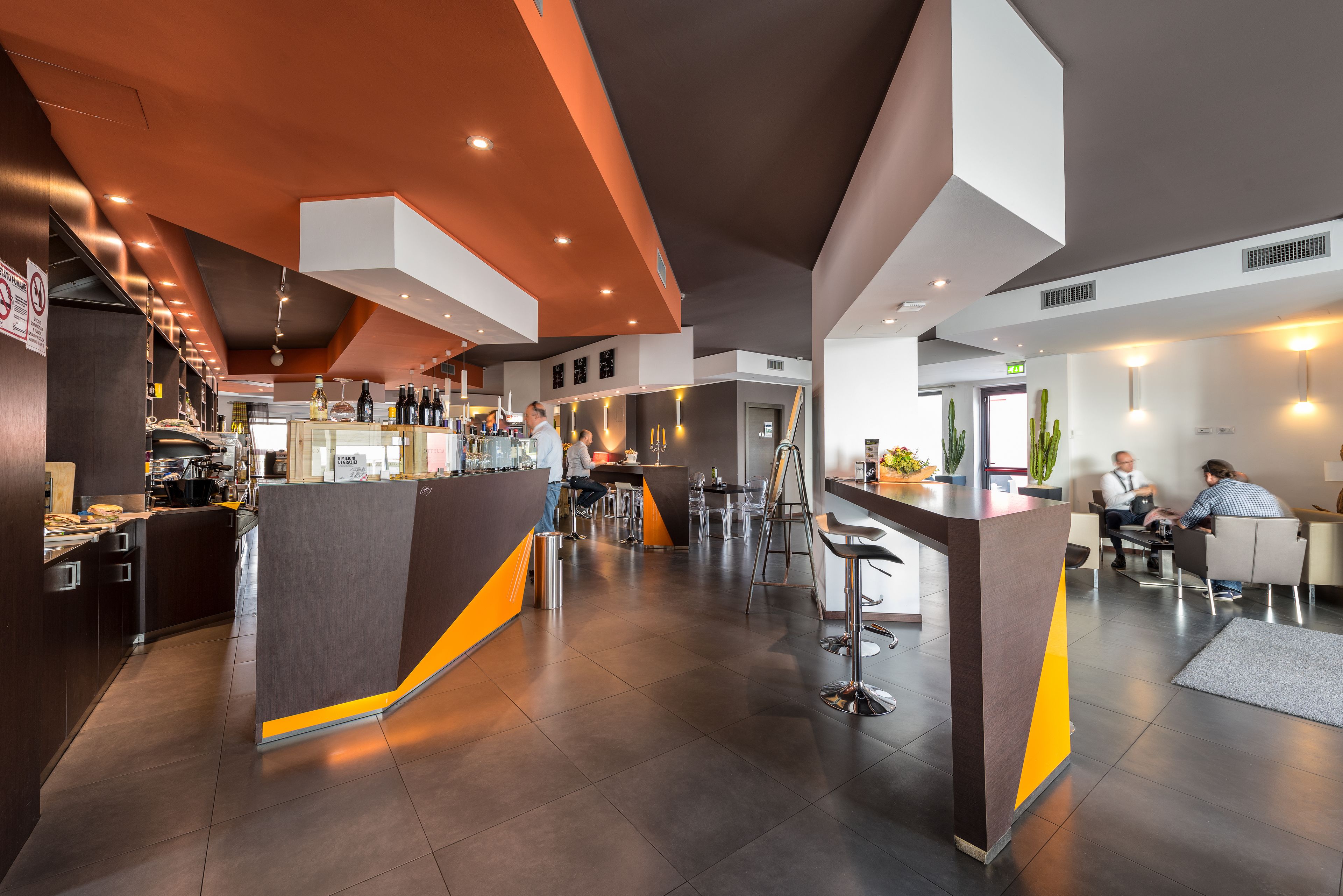 Un bar moderno con barra, taburetes y zona de estar con mesas y sillas.