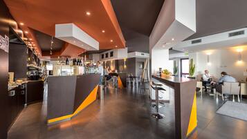 Un bar moderno con barra, taburetes y zona de estar con mesas y sillas.