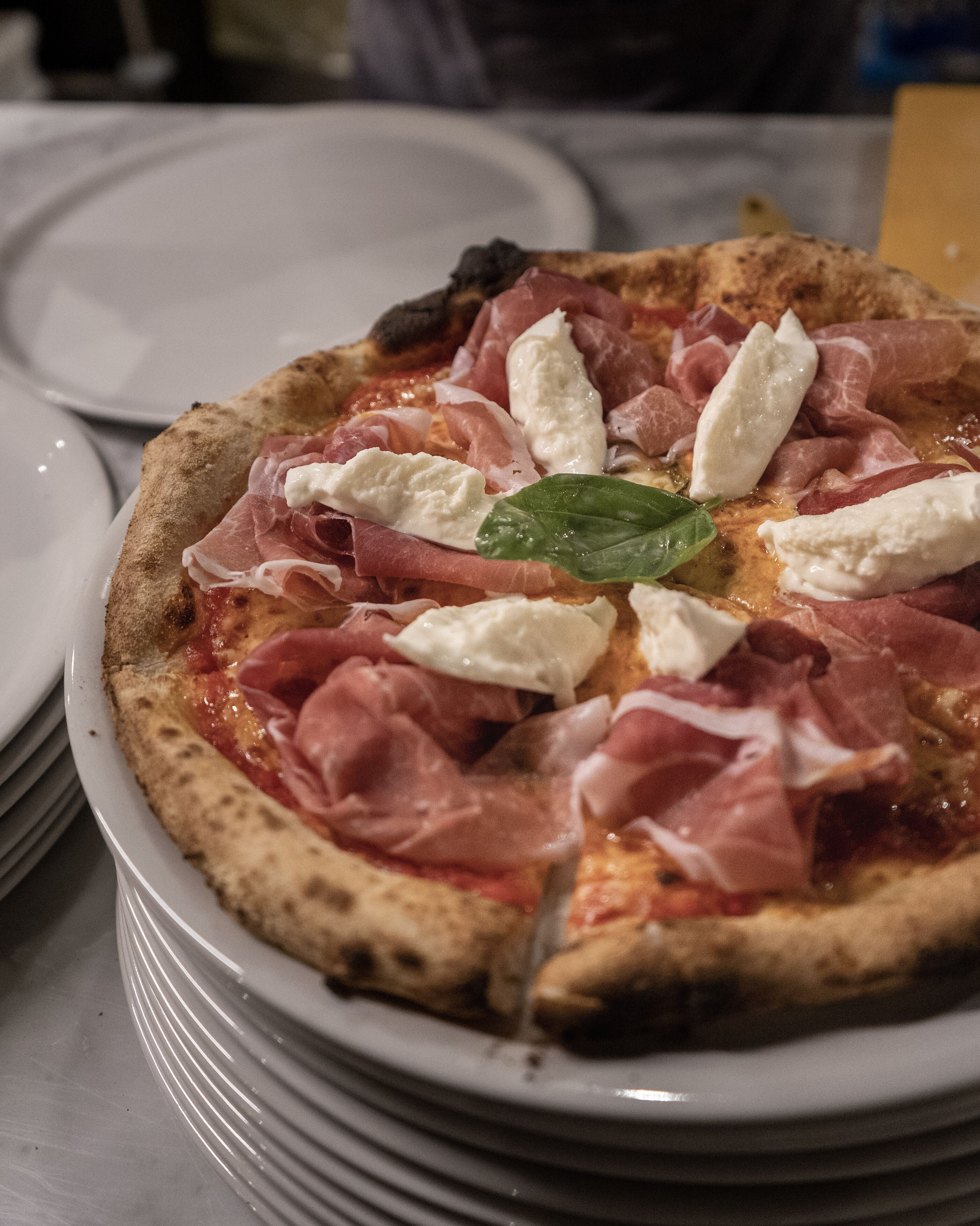Una pizza con jamón serrano y mozzarella sobre un plato.