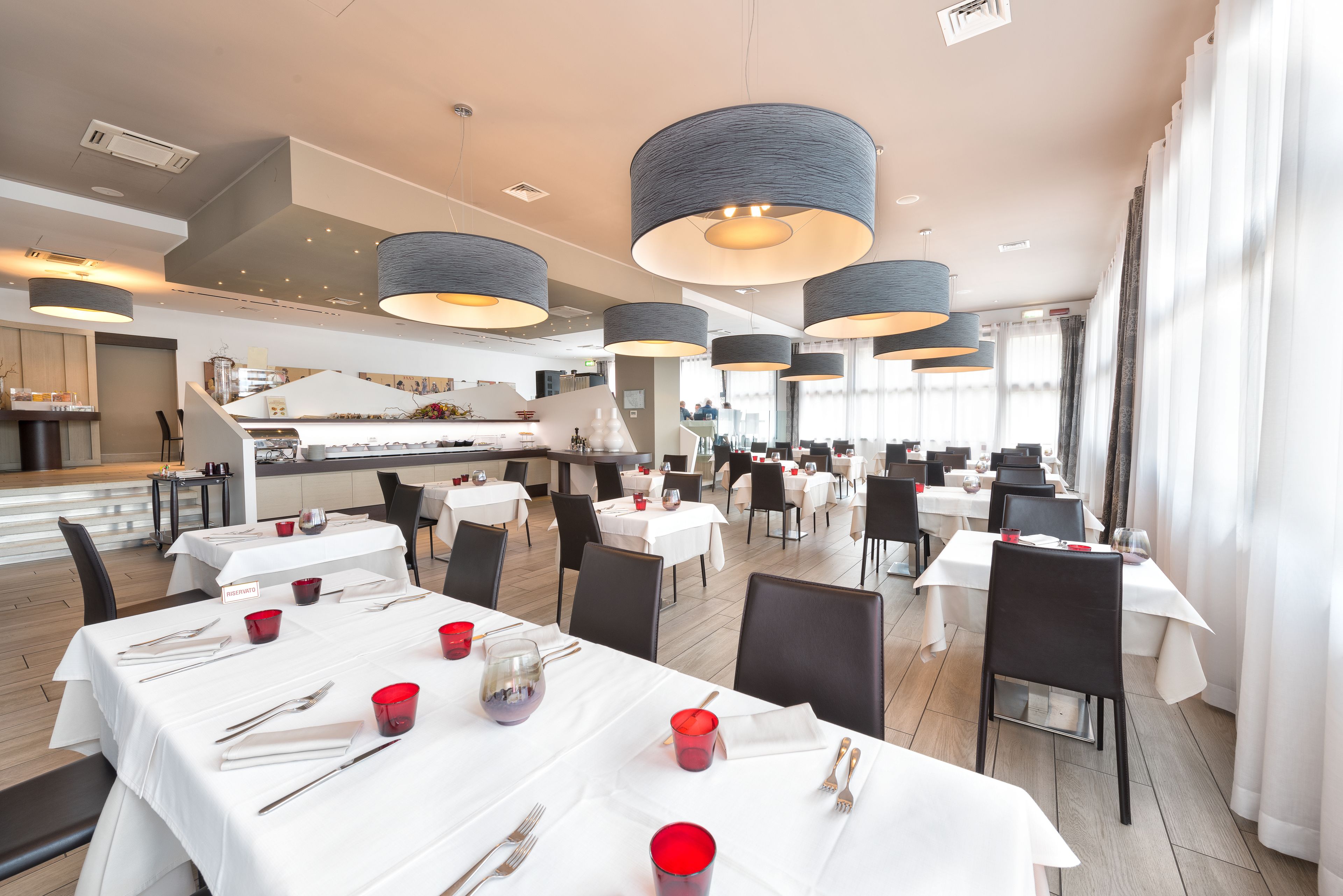 A spacious restaurant with multiple dining tables, black chairs, and modern pendant lighting.