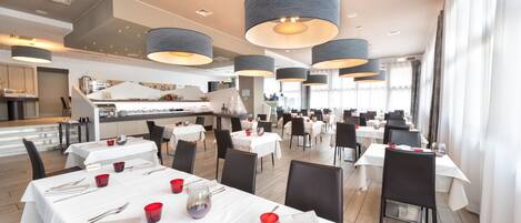 A spacious restaurant with multiple dining tables, black chairs, and modern pendant lighting.