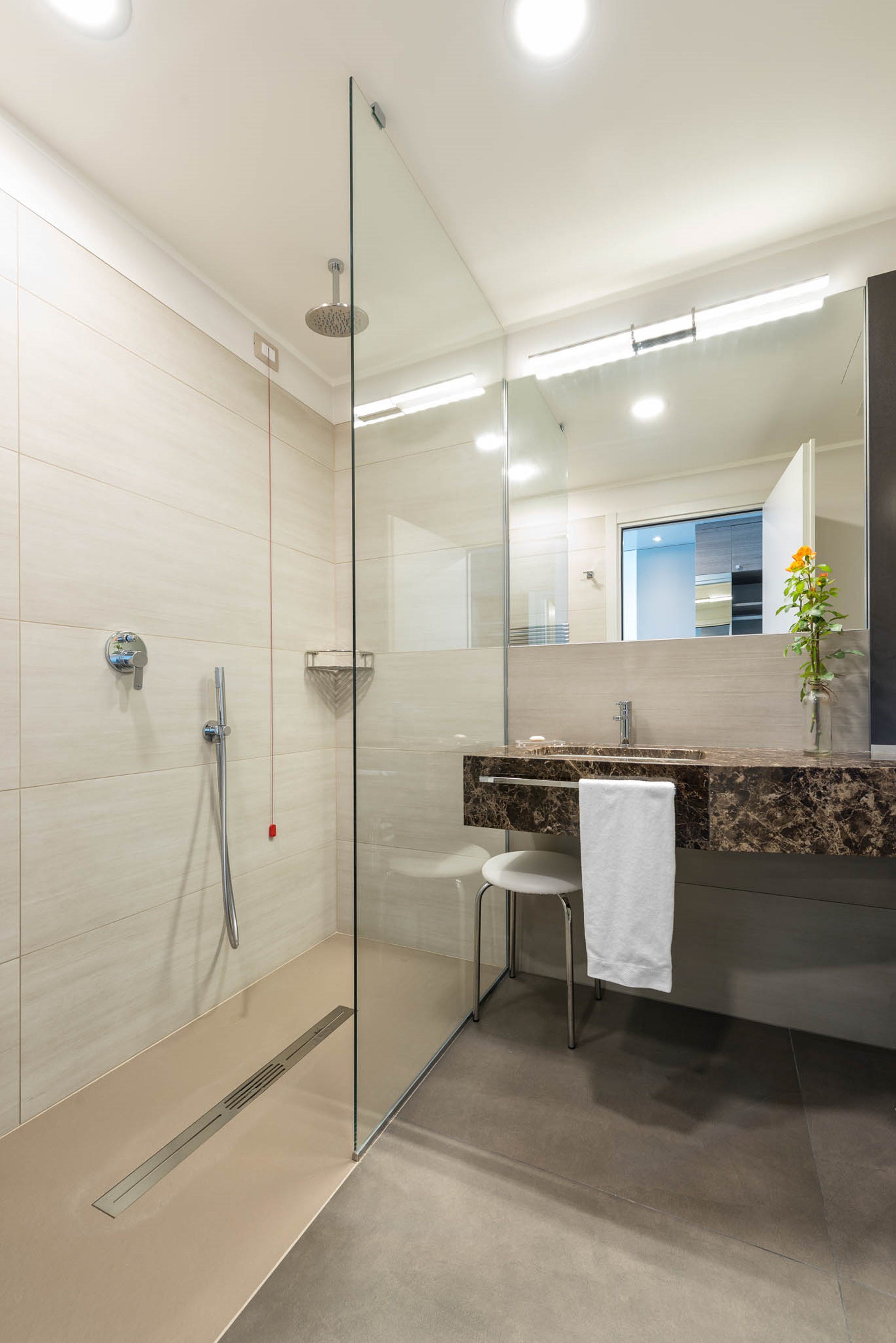 A modern bathroom with a glass shower enclosure, a marble sink, and a large mirror.