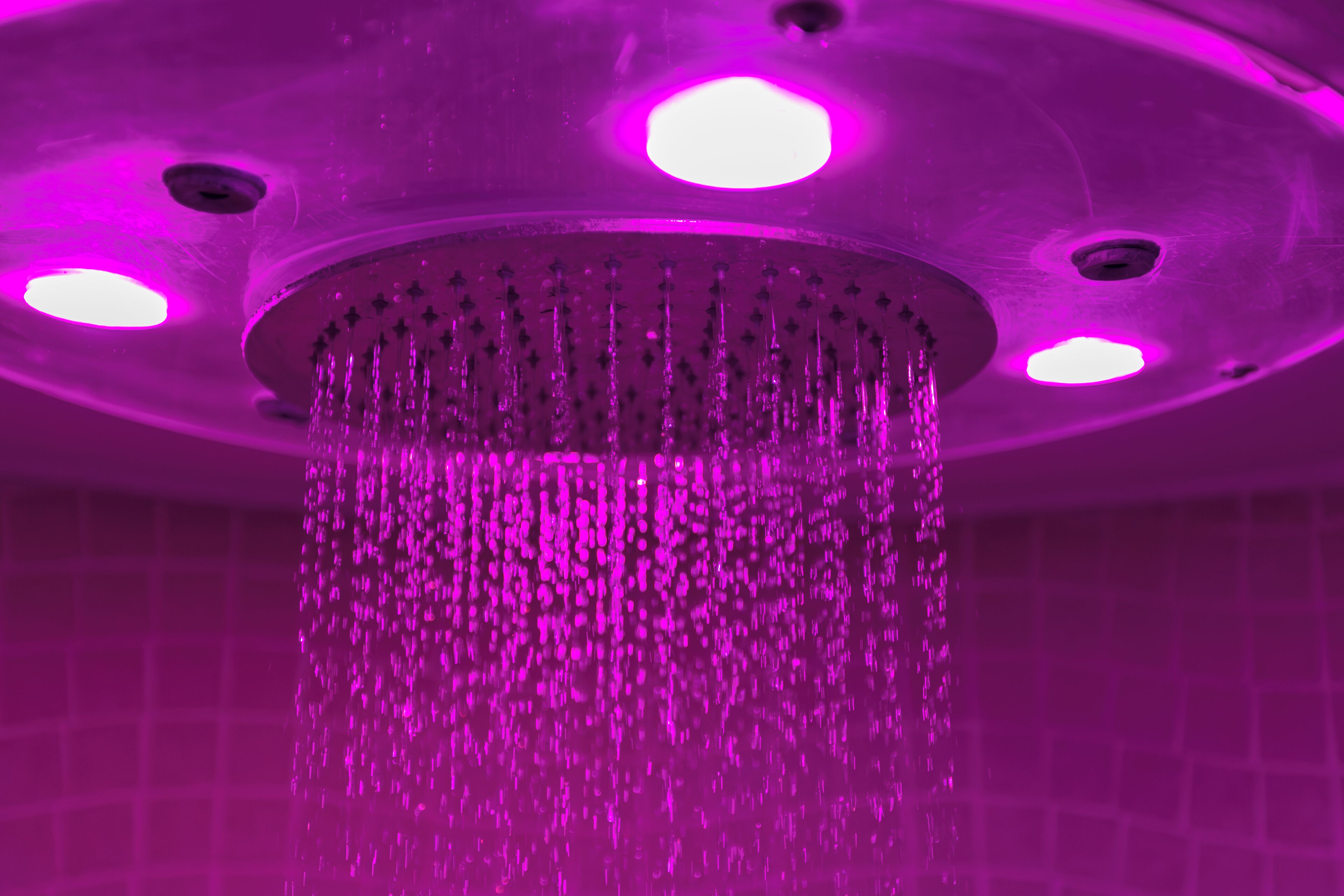 A showerhead with multiple nozzles and a circular design, set against a tiled wall.