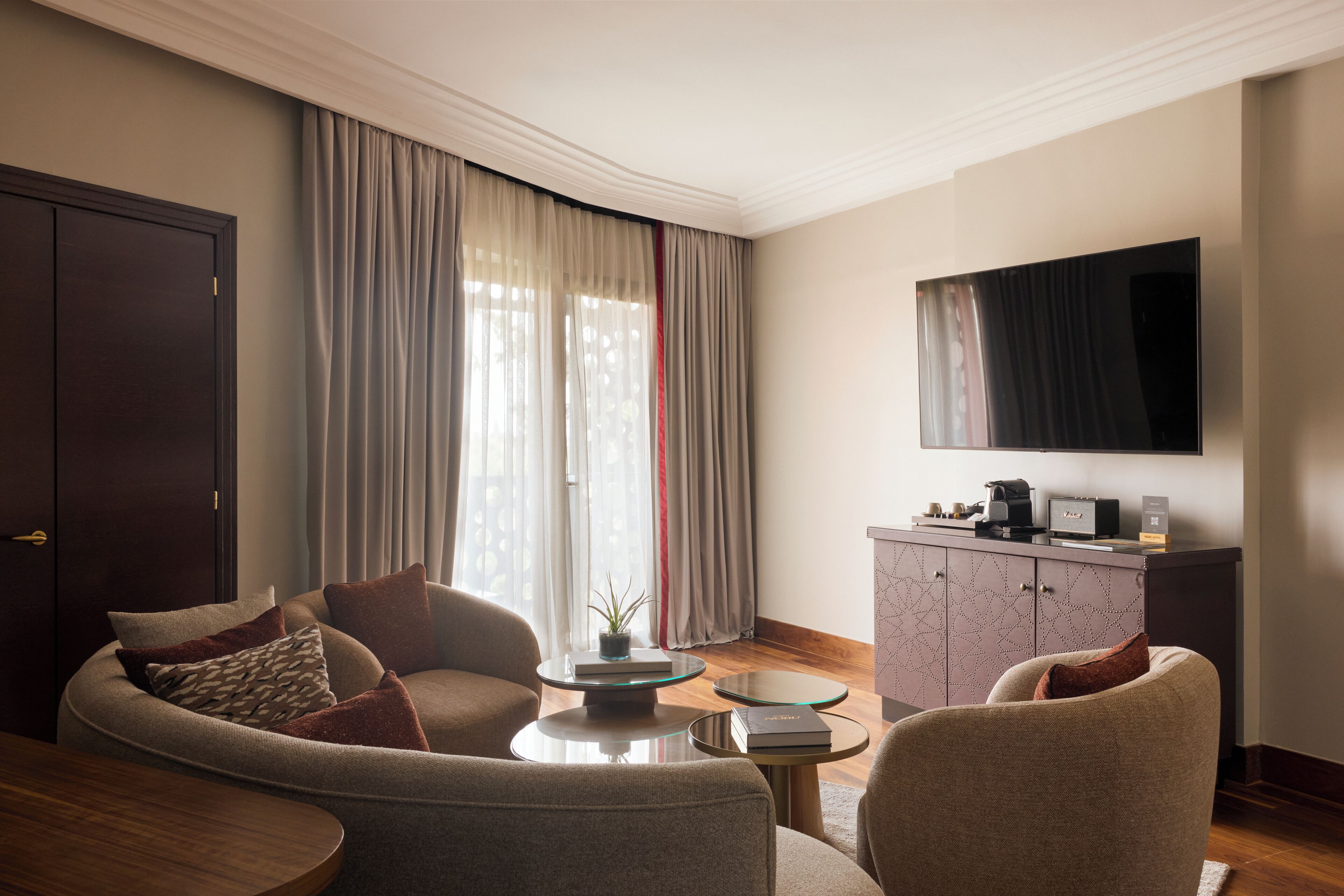 A modern living room with a sofa, armchairs, a coffee table, and a flat-screen TV mounted on the wall.