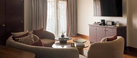 A modern living room with a sofa, armchairs, a coffee table, and a flat-screen TV mounted on the wall.