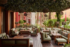 An outdoor seating area with multiple sofas and tables, surrounded by greenery and palm trees.