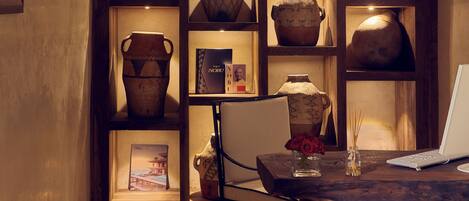 A dining area with a wooden table, chairs, and a laptop. Shelves behind the table display various pottery items.