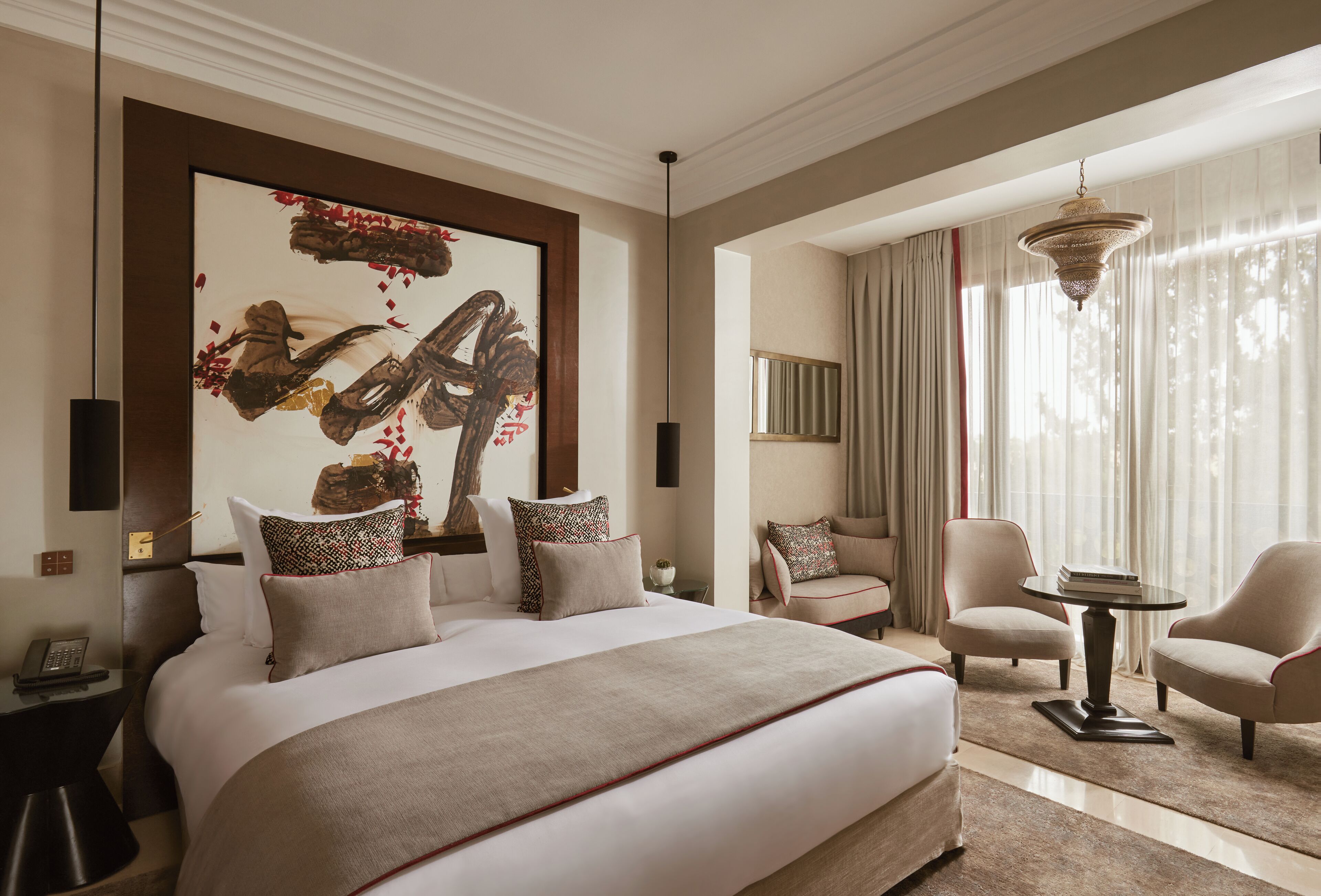 A spacious hotel room with a large bed, a sitting area with two armchairs, a small table, and a large abstract painting on the wall.