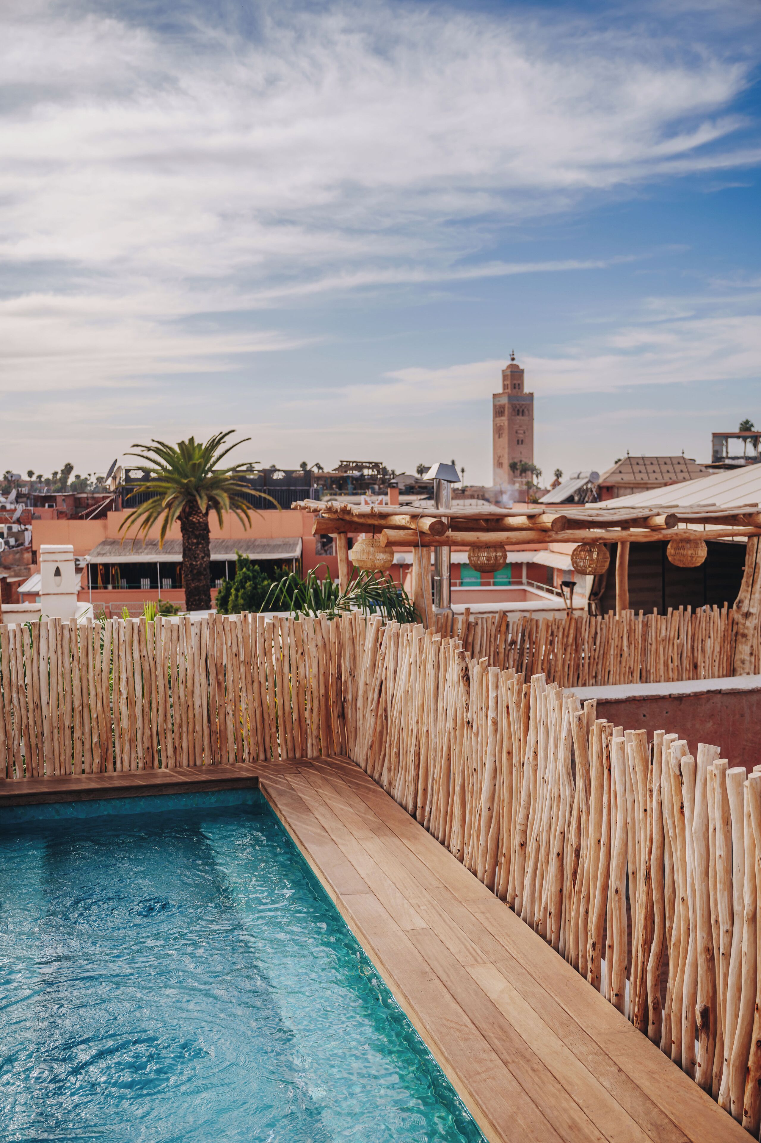 A swimming pool with wooden decking and a palm tree, surrounded by a wooden fence.