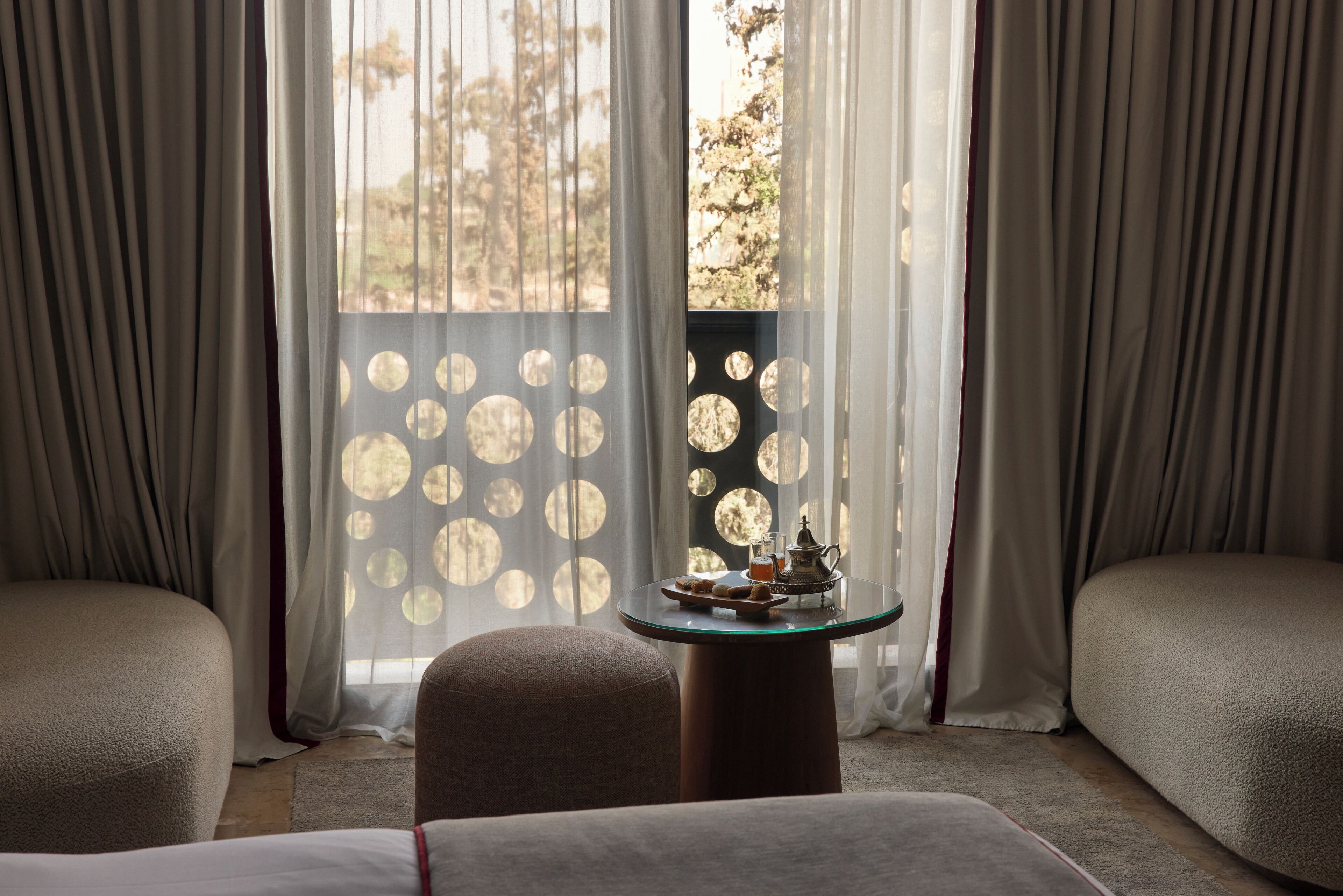 Ein Hotelzimmer mit einem runden Glastisch, zwei Sofas und Blick durch ein Fenster mit kreisförmigen Mustern.