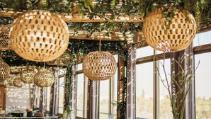 Un interno di ristorante con mobili in vimini, lampade sferiche a sospensione e ampie finestre.