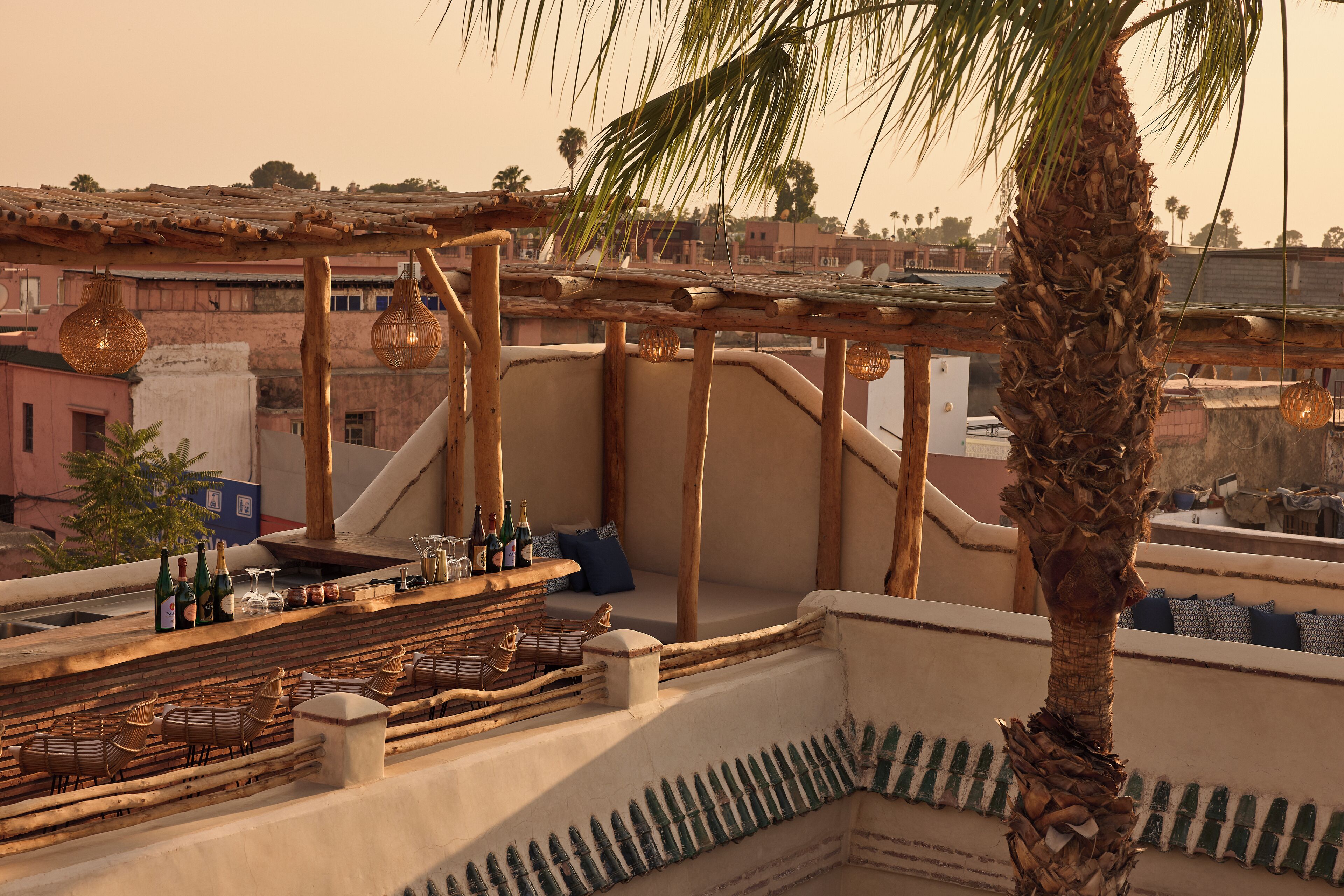 A rooftop terrace with seating, a bar area with bottles, and a palm tree.