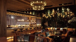 Angolo bar dal design moderno, con bancone, posti a sedere e parete decorata con piante e illuminazione.