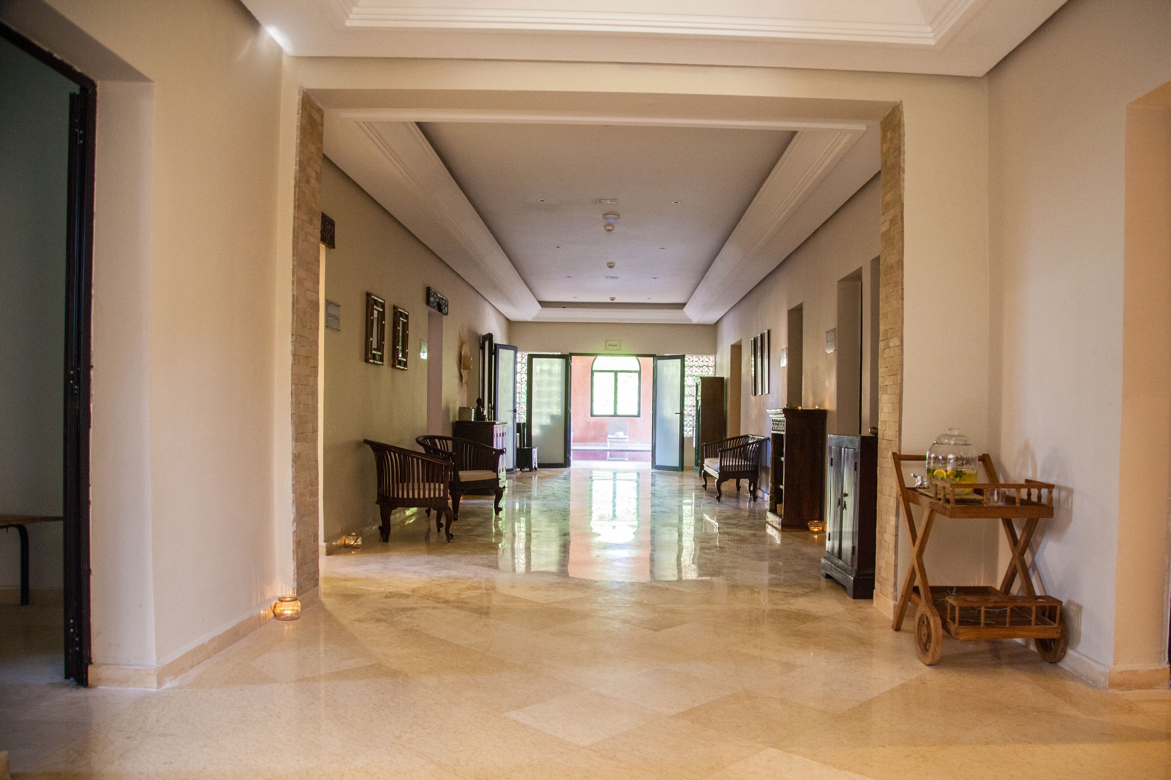 A spacious hallway with a polished floor, a wooden bench, and a cart with glassware.