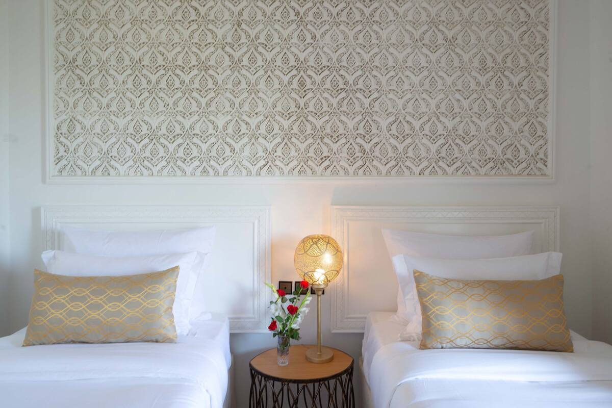 Une chambre d’hôtel avec deux lits, une table ronde avec une lampe et un mur décoré de motifs.