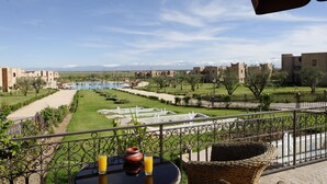 Un balcón con vista a una piscina, jardín y montañas distantes.