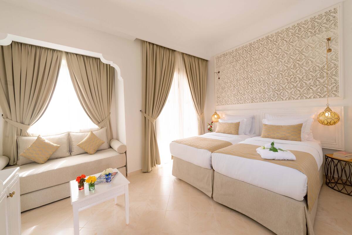Une chambre d’hôtel avec un canapé, un lit, une petite table ornée de fleurs et un mur à motifs.