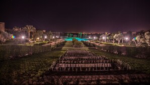 Vista nocturna de un jardín formal con diseño geométrico, una fuente central e iluminacion en los senderos.