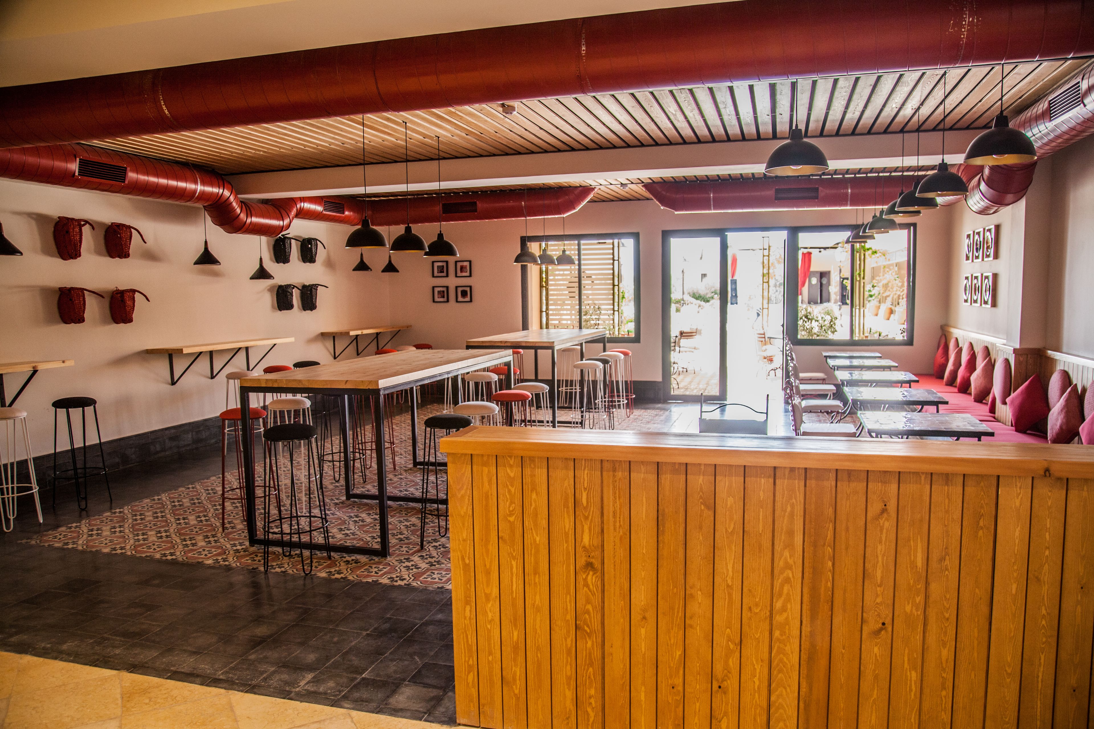 Een restaurant met een houten bar, meerdere tafels en stoelen. Er zijn hanglampen en een groot raam met uitzicht.