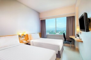 A hotel room with two beds, a desk with a chair, a TV, and a window with a city view. - favehotel Manahan - Solo (Surakarta)