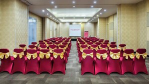 Une salle de conférence avec des rangées de chaises rouges ornées de rubans dorés, un pupitre et un écran de présentation.