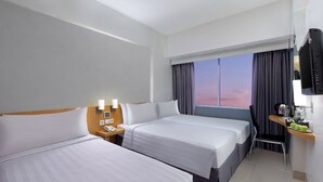 Une chambre d’hôtel avec deux lits, un bureau avec une chaise, une télévision et une fenêtre avec des rideaux.